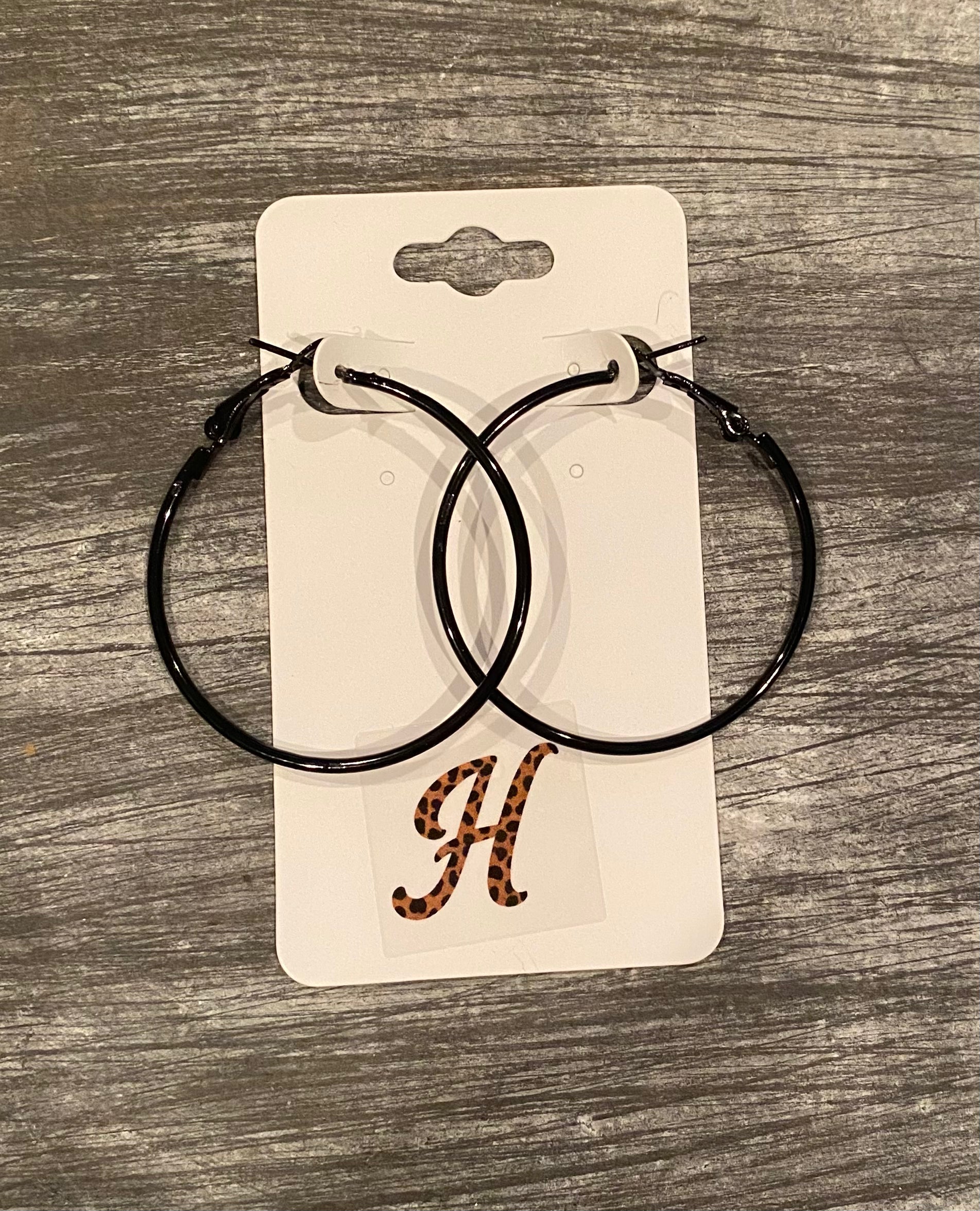Black hoop earrings on a branded card with a 'H' logo on a wooden surface
