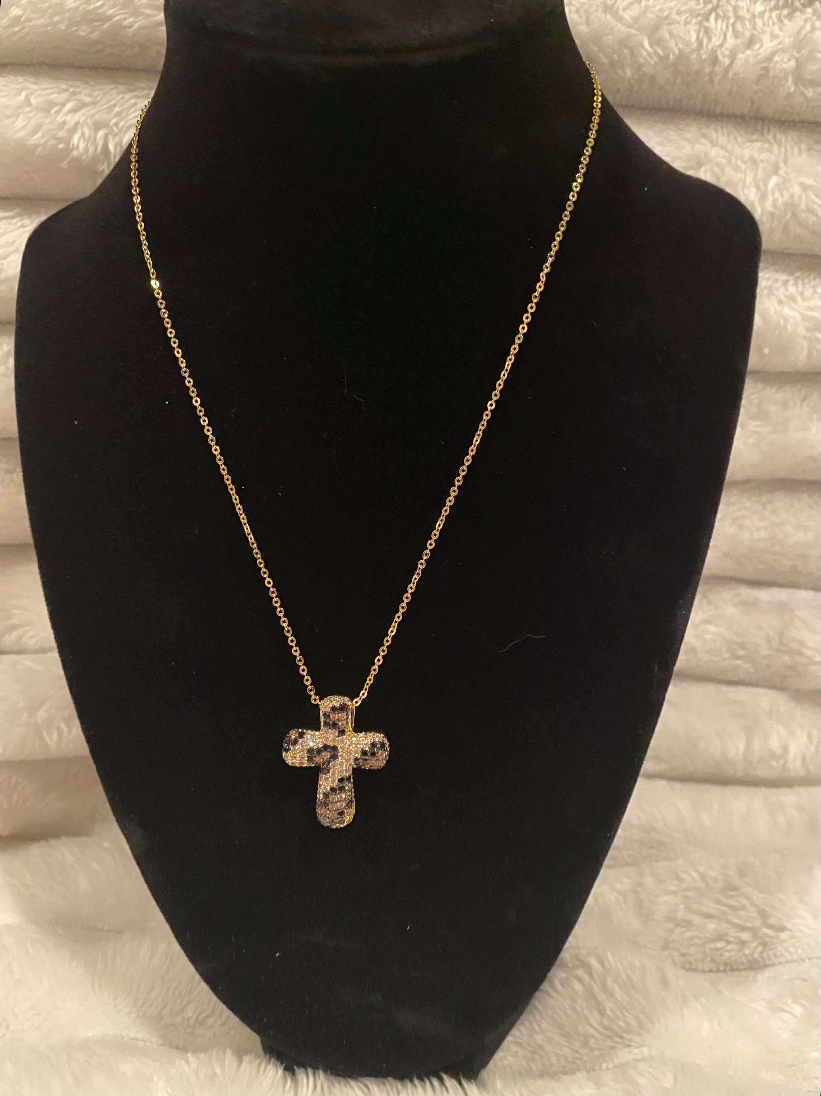 Gold cross necklace on a black mannequin bust with a neutral background
