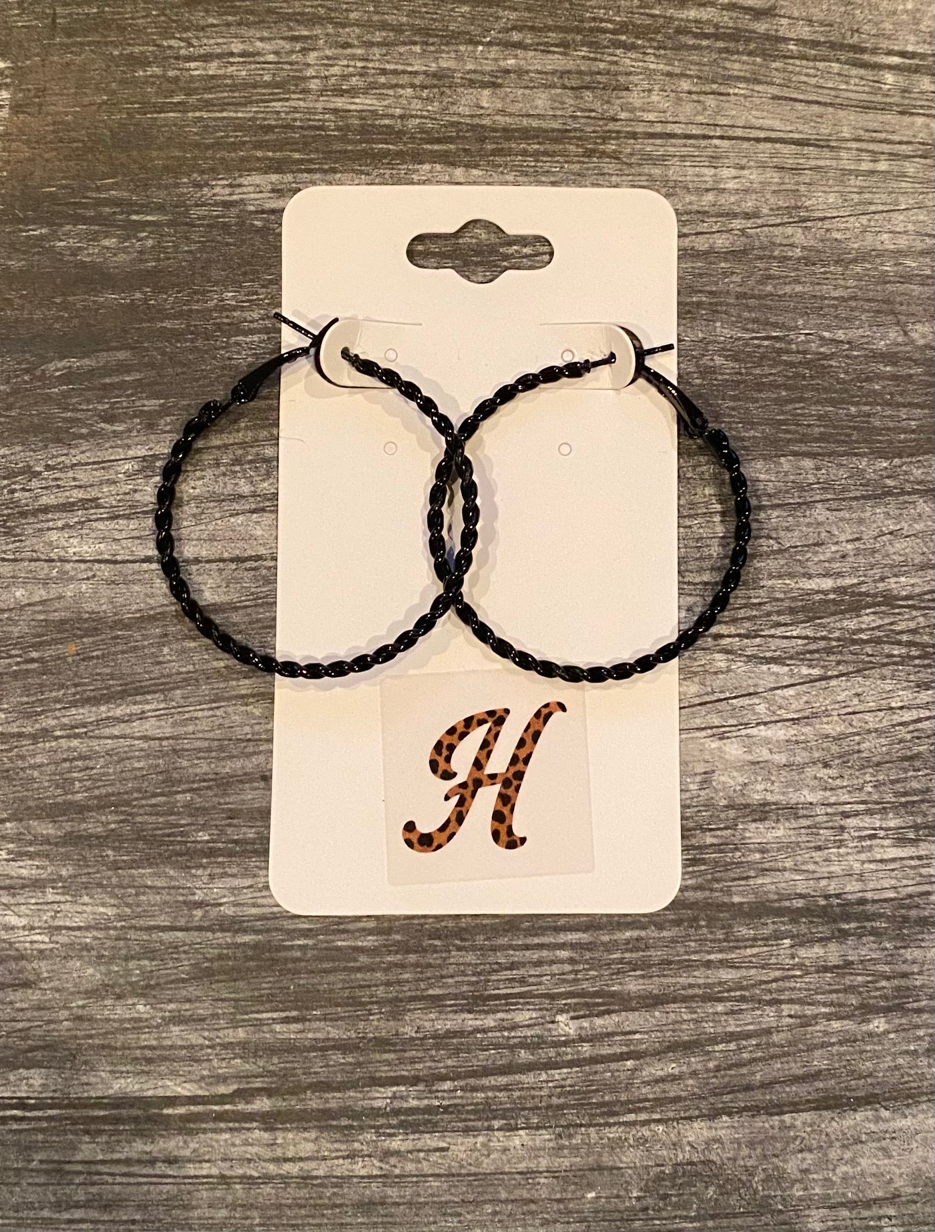 Black hoop earrings on a beige card with a letter 'H' on a wooden surface