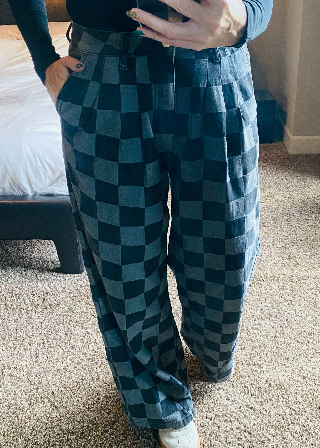 Person wearing checkered pants taking a mirror selfie in a room.