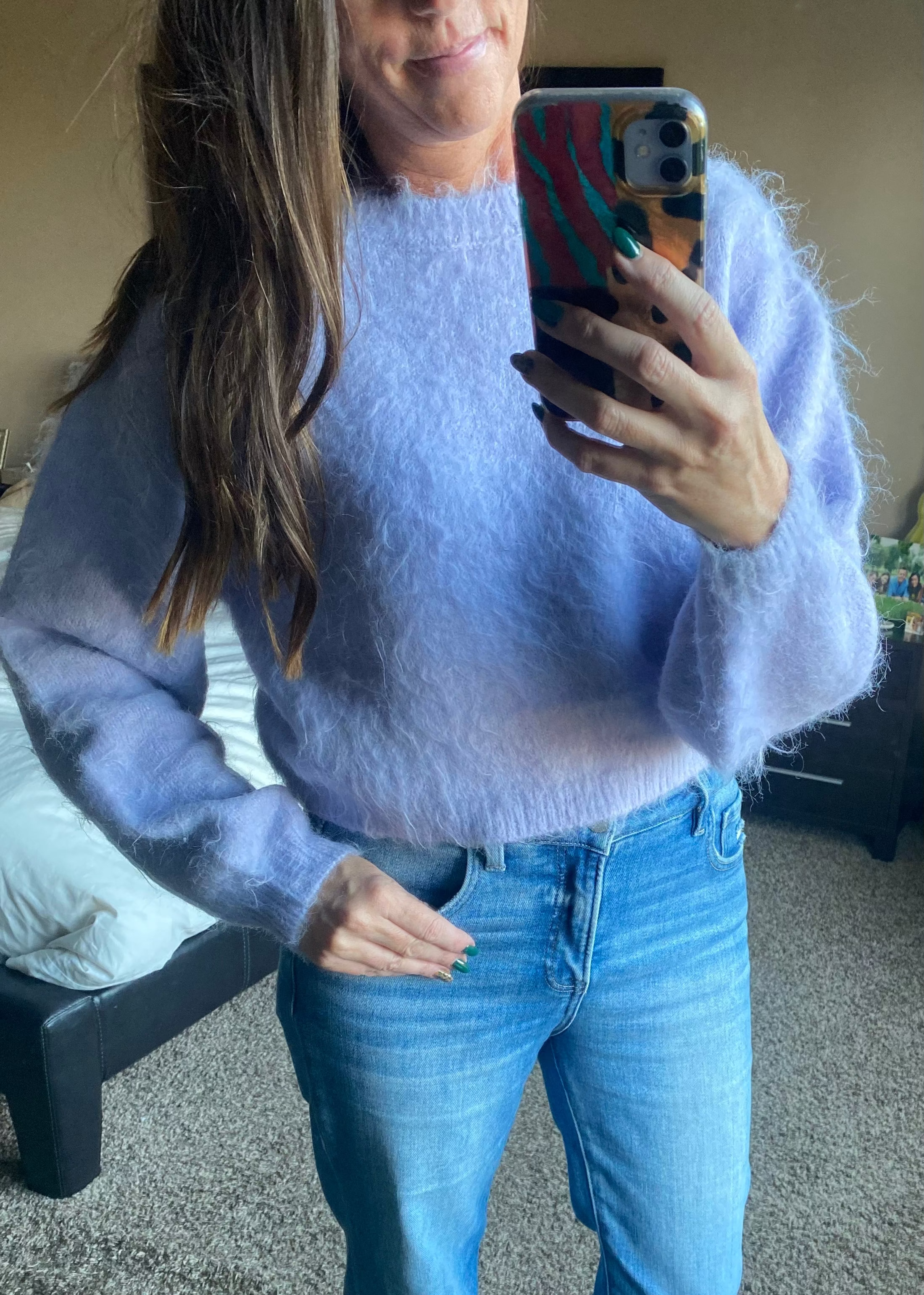 Person wearing a light purple sweater and blue jeans taking a mirror selfie.