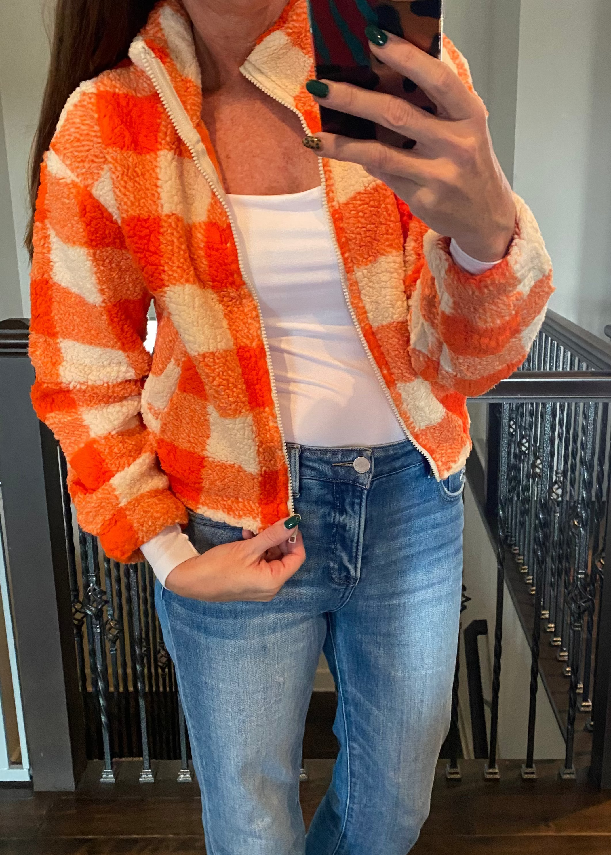 Person wearing an orange and white checkered jacket, white shirt, and blue jeans taking a mirror selfie.