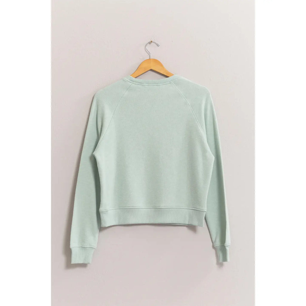 Mint green sweatshirt on a wooden hanger against a light gray background