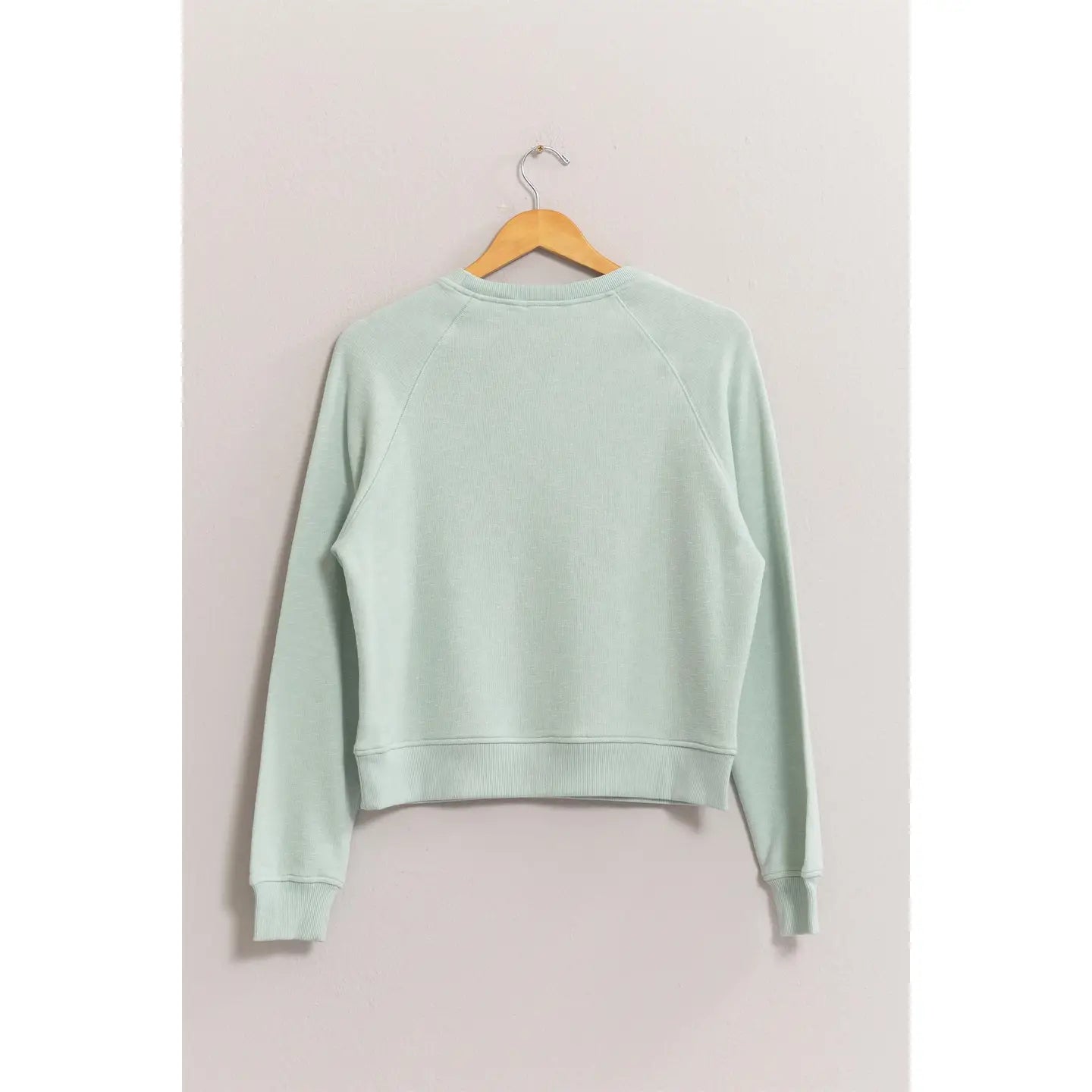 Mint green sweatshirt on a wooden hanger against a light gray background