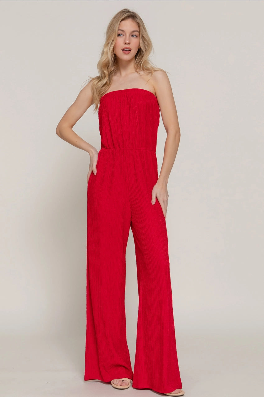 Woman wearing a red strapless jumpsuit on a plain background