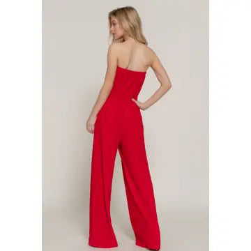 Woman wearing a red strapless jumpsuit on a plain background