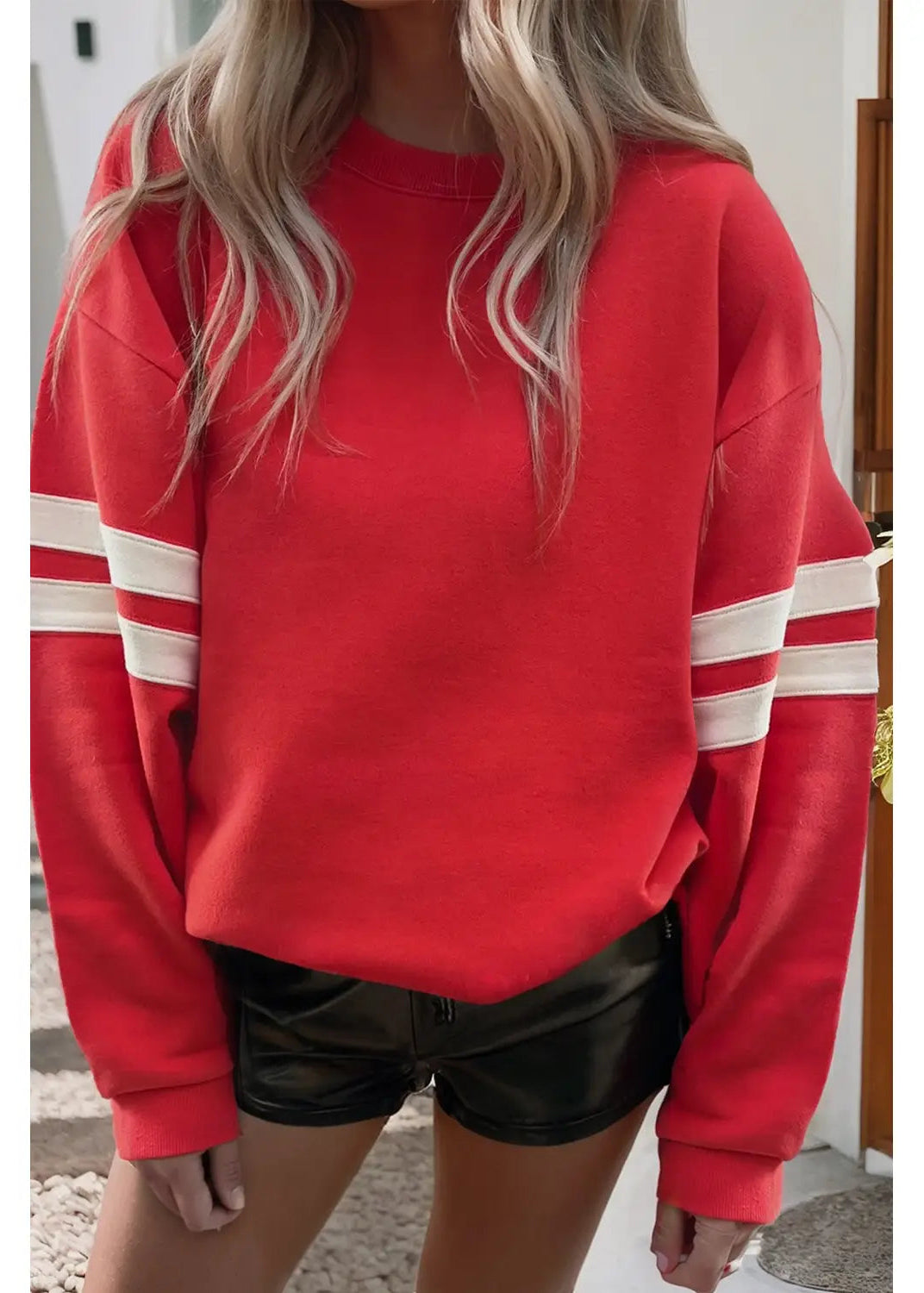 Person wearing a red sweatshirt with white stripes and black shorts.